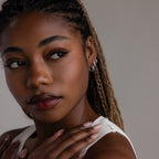 Woman with braided hair wearing silver hoop earrings against a neutral background