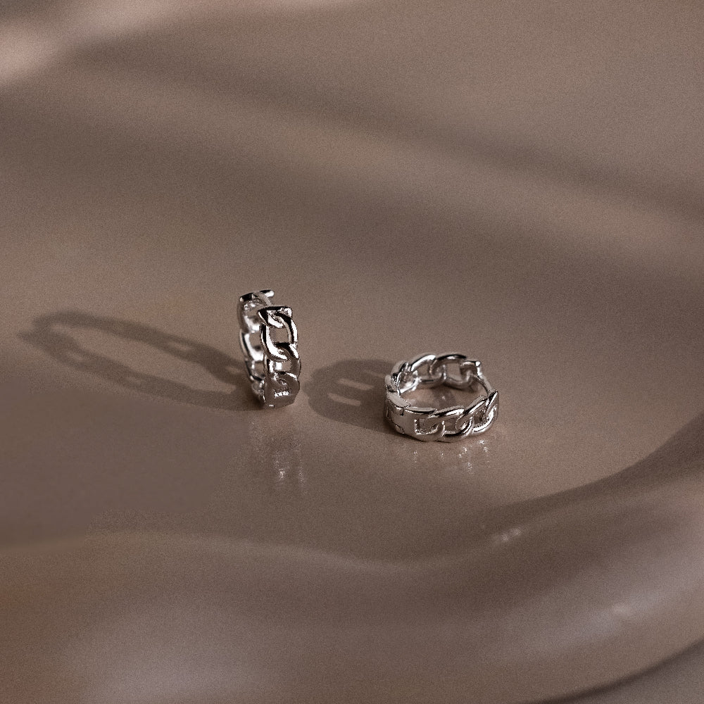 Two silver chain-style hoop earrings on a beige surface