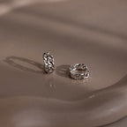 Two silver chain-style hoop earrings on a beige surface