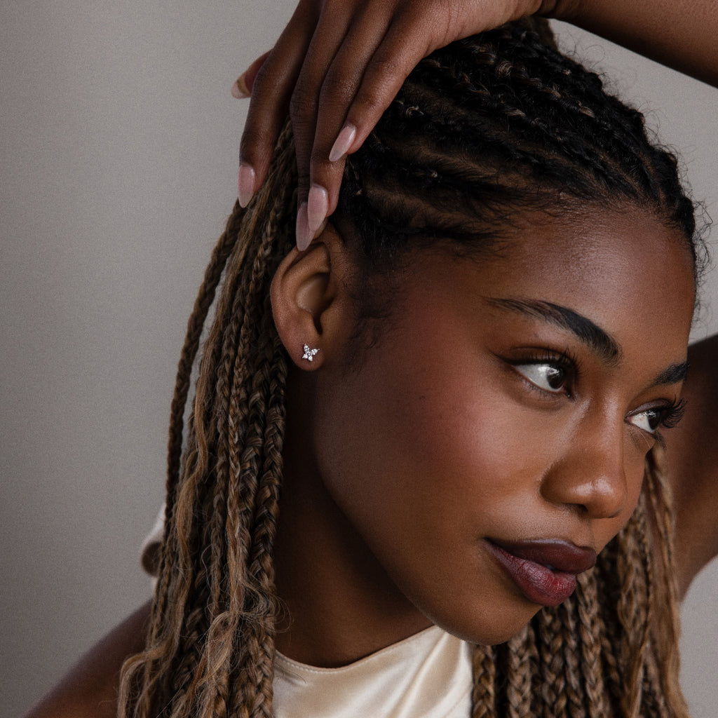 Woman with braided hair wearing a small diamond butterfly earring, looking to the side.