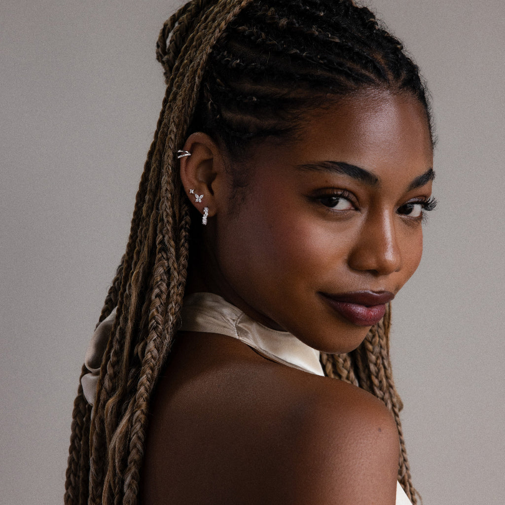 Woman with braided hair wearing various diamond earrings against a neutral background