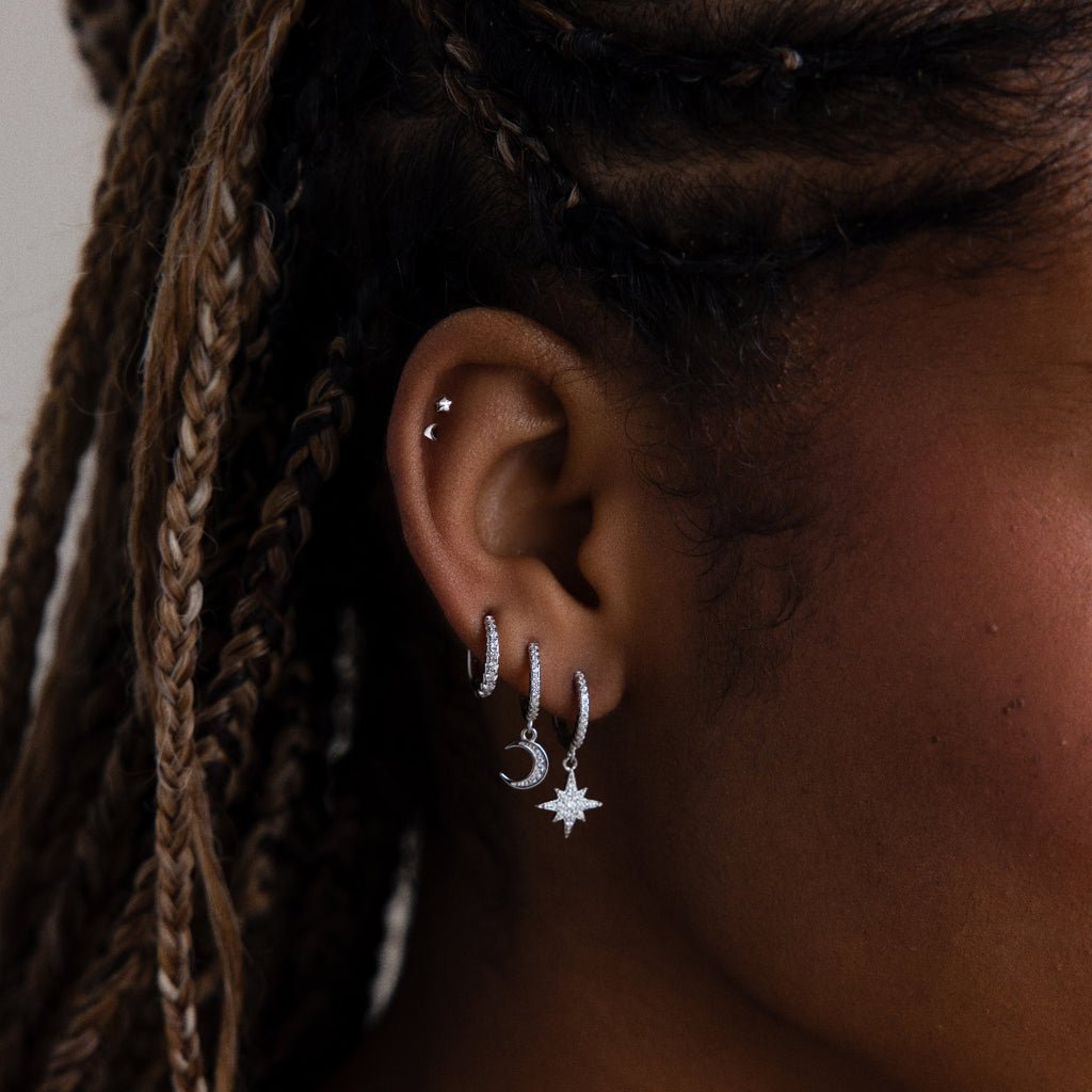 Close-up of an ear with silver hoop earrings and star-shaped earrings.
