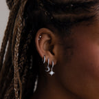 Close-up of an ear with silver hoop earrings and star-shaped earrings.
