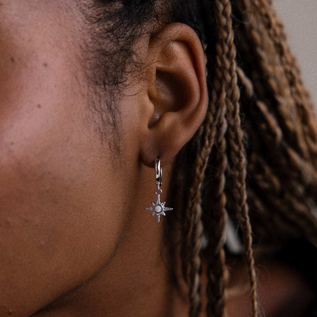 Close-up of a model wearing a silver star-shaped opal huggie hoop earring with braided hair.