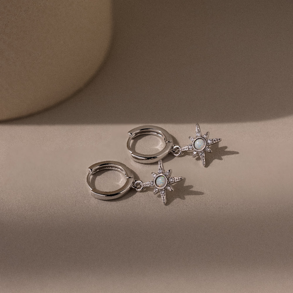 Pair of silver pave opal earrings with star designs on a beige background