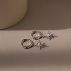 Pair of silver pave opal earrings with star designs on a beige background