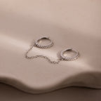Pair of silver diamond hoop earrings with a chain on a beige surface