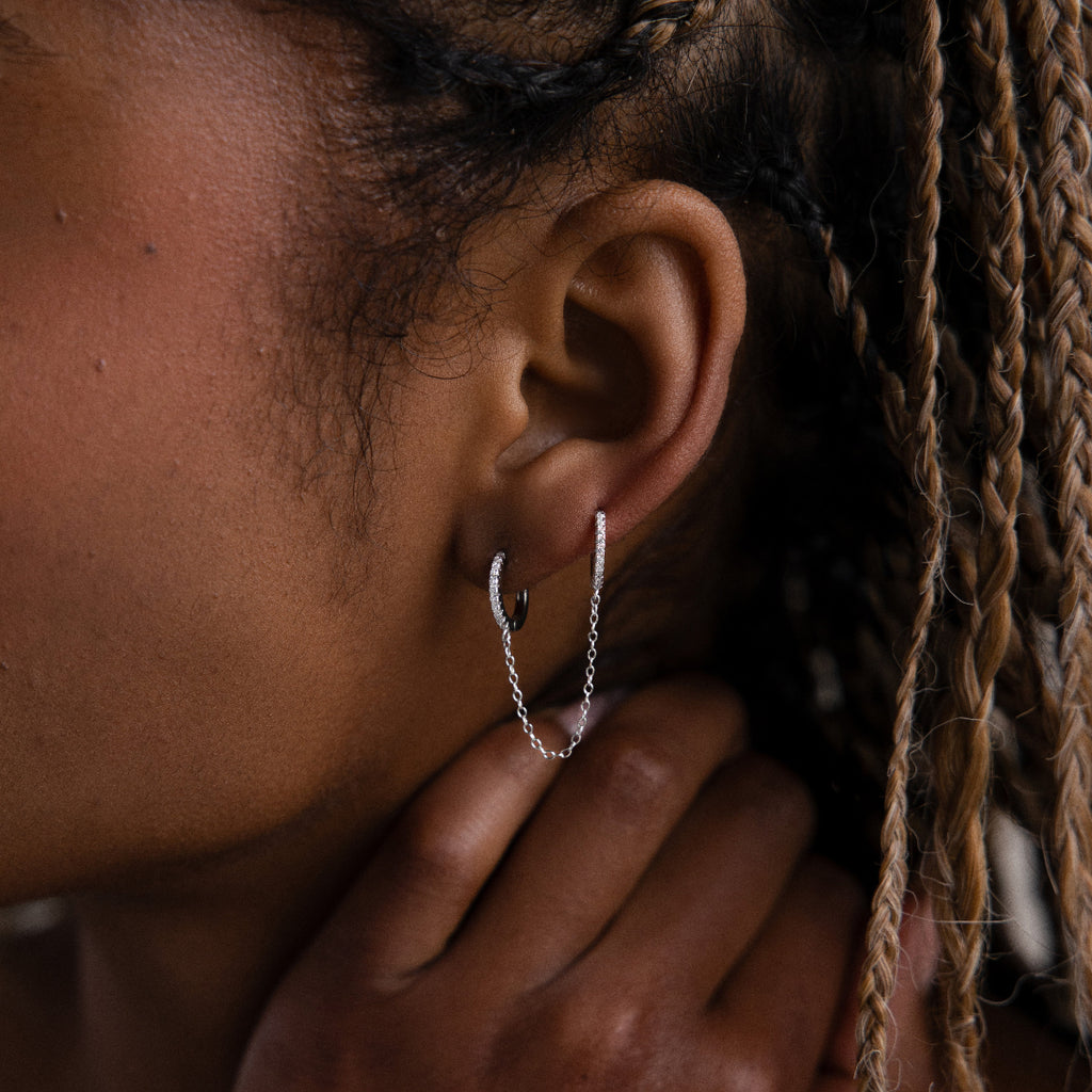 Close-up of a model with a silver double hoop chain earring, hand touching the face, and braided hair.