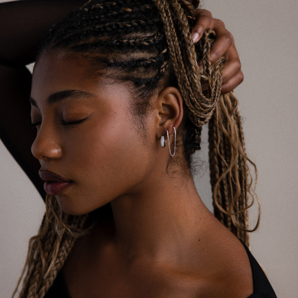 Woman with braided hair wearing silver hoop earrings against a neutral background
