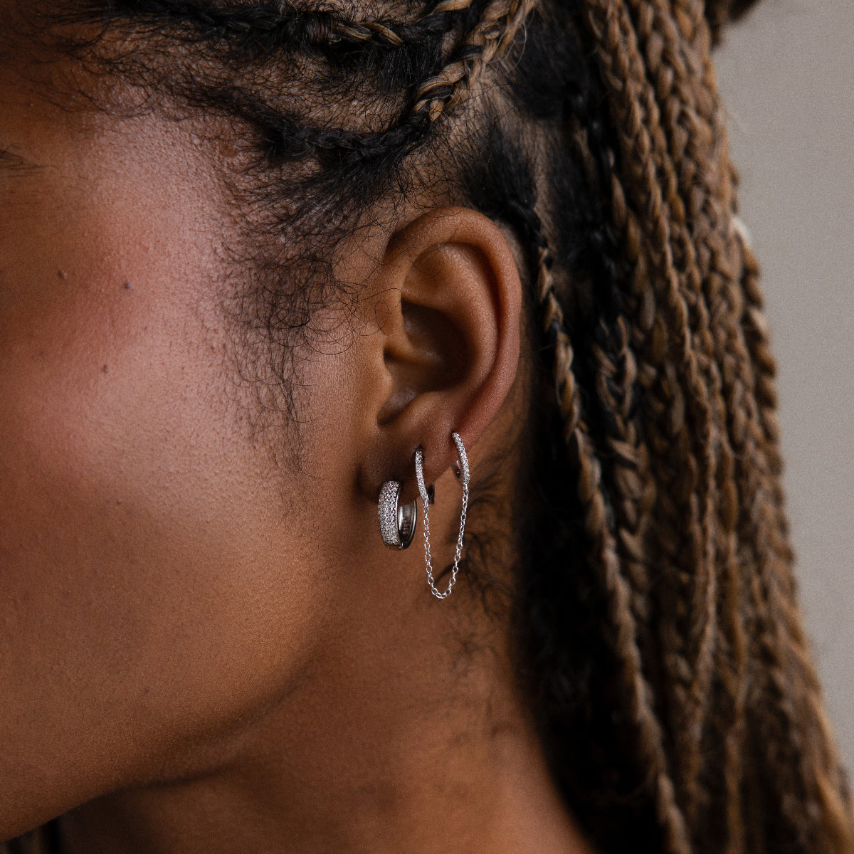Close-up of a model with silver double hoop earrings connected by a chain and braided hair.