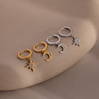 Two pairs of gold and silver hoop earrings with star and moon charms on a beige surface