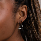 Close-up of an model wearing silver hoop earrings with star and moon designs.