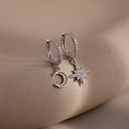 Silver hoop earrings with star and moon charms on a beige surface