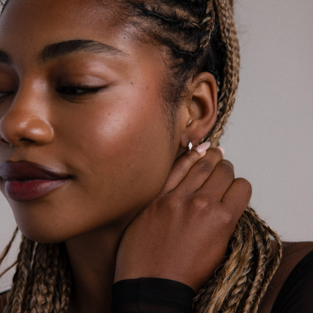 Woman adjusting a small silver diamond hoop earring with a neutral background