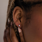 Close-up of a model with a silver diamond stud earring, hand brushing against her face.