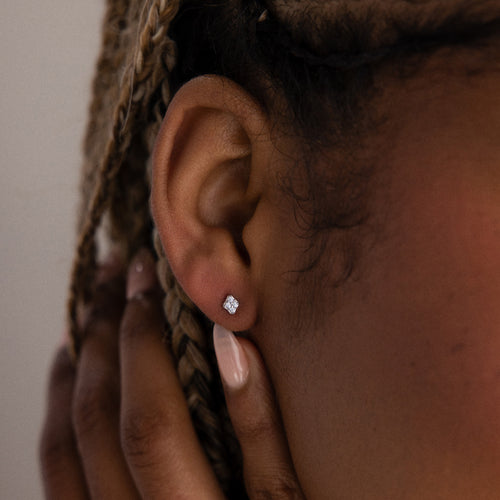 Close-up of a model with a silver diamond stud earring, hand brushing against her face.