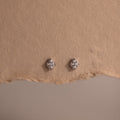 Pair of silver diamond stud earrings on a textured brown surface