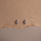 Pair of silver diamond stud earrings on a textured brown surface