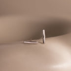 Pair of silver bar stud earrings on a beige surface with a neutral background