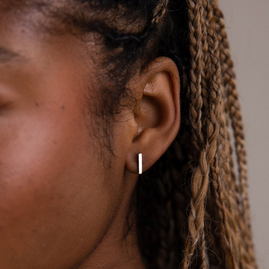Close-up of a model with a minimalistic silver bar earring, hair styled in braids.
