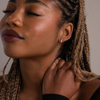 Close-up of a woman with a silver stud earring and braided hair touching her neck against a neutral background