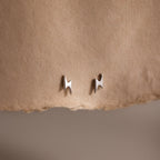 Pair of silver lightning bolt stud earrings on a beige fabric background