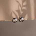 Close-up of a beige fabric with round metallic silver hoop earrings on a neutral background