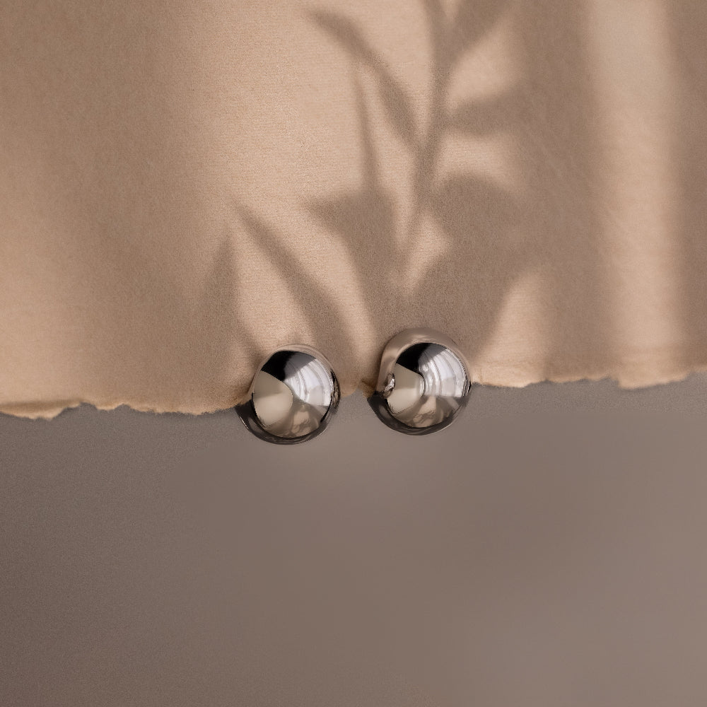 Close-up of a beige fabric with round metallic silver hoop earrings on a neutral background