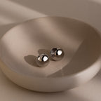 Two round silver earrings on a beige dish with a neutral background