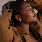 Woman wearing a brown pinstripe coat and a silver hoop dome earring with braided hair, close-up shot.