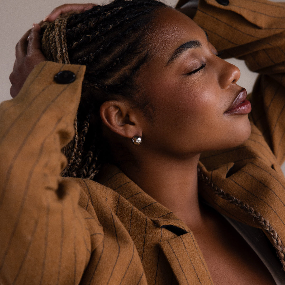 Woman wearing a brown pinstripe coat and a silver hoop dome earring with braided hair, close-up shot.