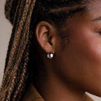 Close-up of an ear with a silver spherical earring, focusing on the jewelry.