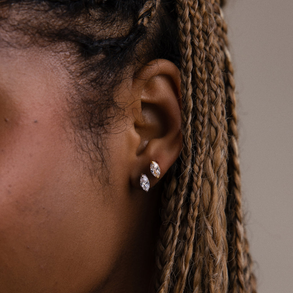Close-up of a model with braided hair wearing two marquise shaped earrings in gold and silver against a neutral background