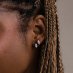 Close-up of a model with braided hair wearing two marquise shaped earrings in gold and silver against a neutral background