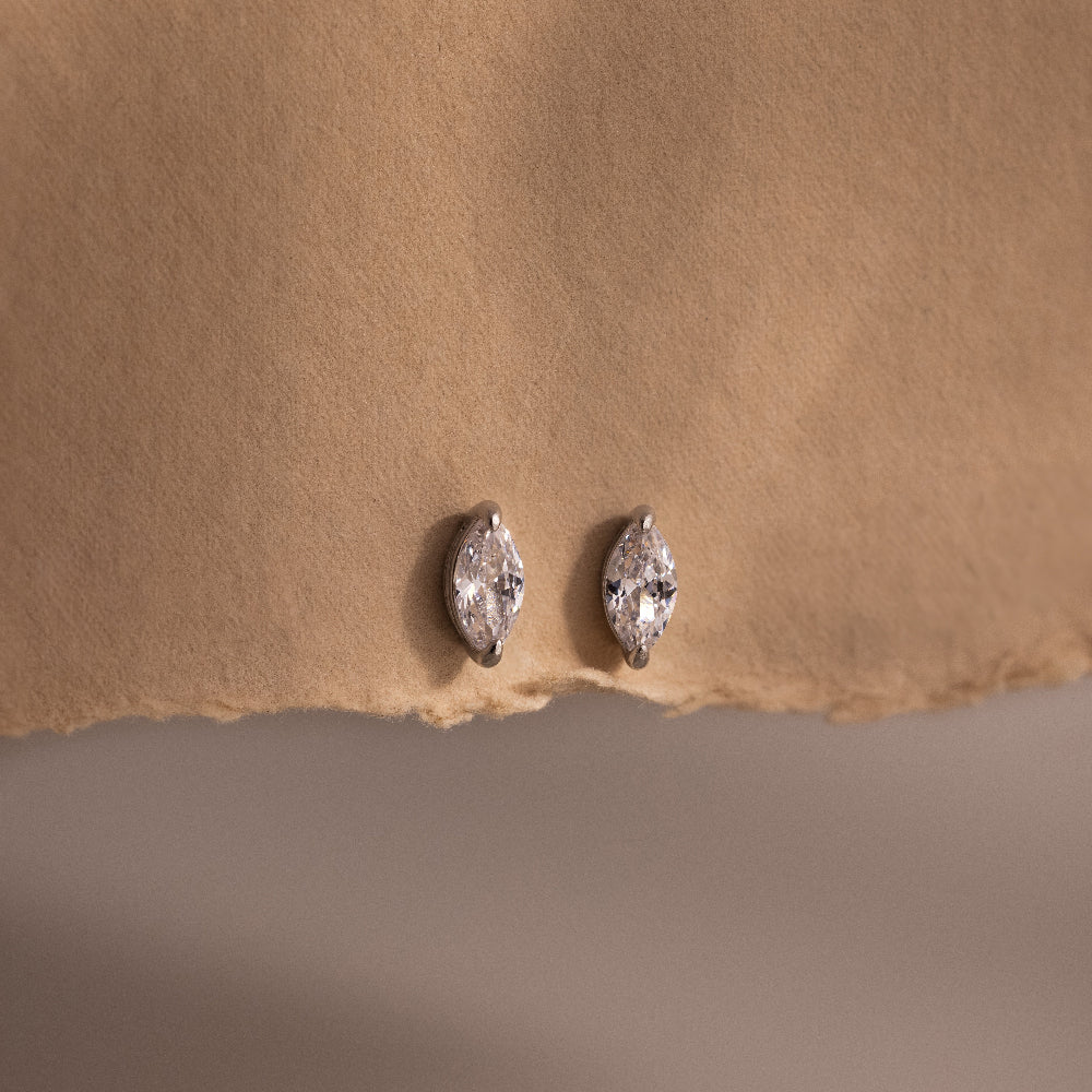 Pair of silver marquise-shaped diamond earrings on a beige fabric background