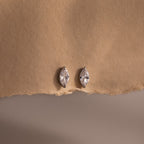 Pair of silver marquise-shaped diamond earrings on a beige fabric background