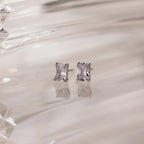 Silver stud earrings with clear rectangular gemstones on a white glass background
