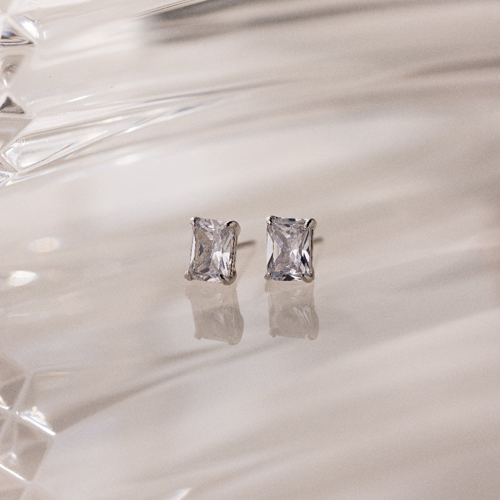 Silver stud earrings with clear rectangular gemstones on a white glass background