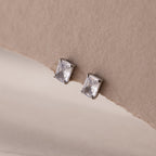 Silver emerald-cut stud earrings on a beige background