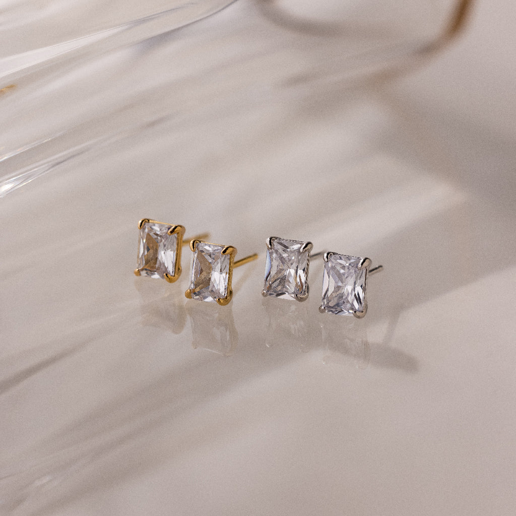 Two pairs of gold and silver stud earrings on a light background