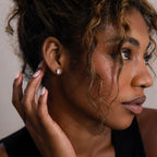 Woman adjusting a silver diamond stud earring with a neutral background
