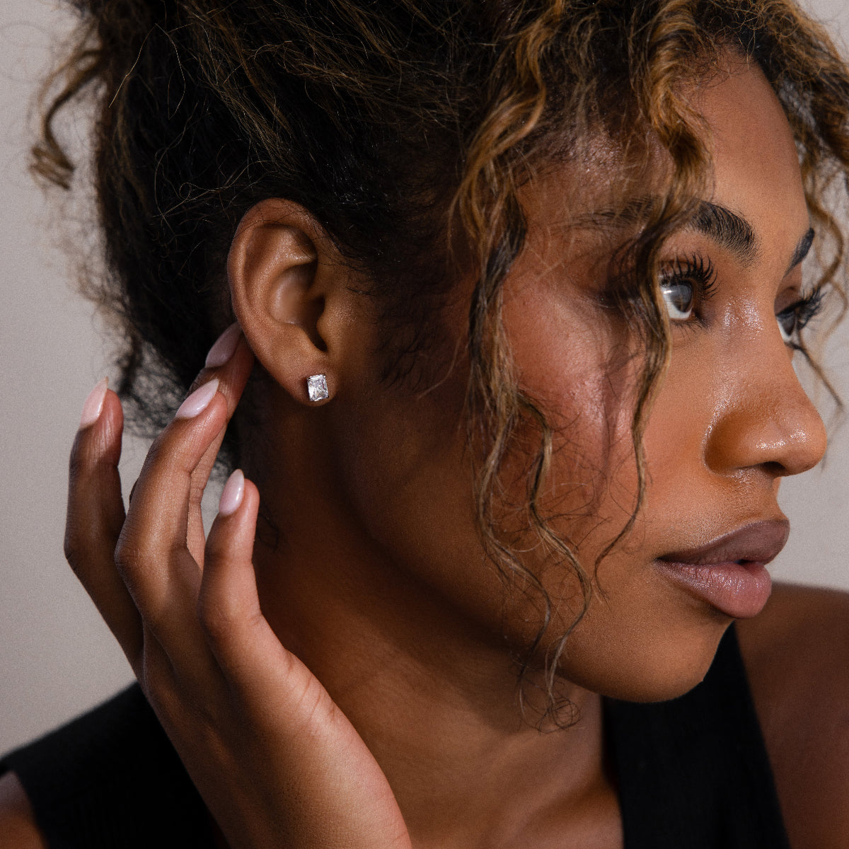 Woman adjusting a silver diamond stud earring with a neutral background