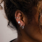 Close-up of a model wearing multiple silver earrings with a neutral background