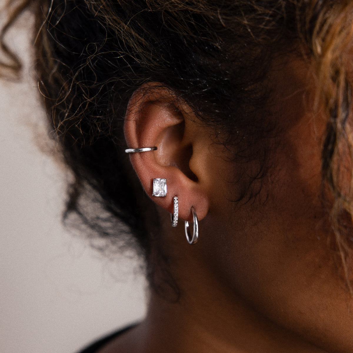 Close-up of a model wearing multiple silver earrings with a neutral background