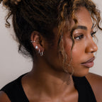 Close-up of a woman wearing various silver earrings with a neutral background