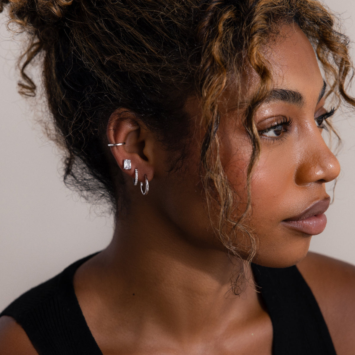 Close-up of a woman wearing various silver earrings with a neutral background