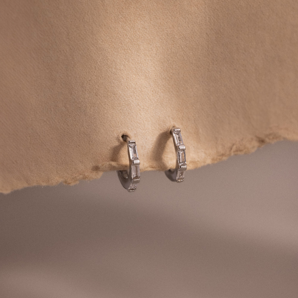 Pair of silver baguette diamond hoop earrings on a beige fabric background