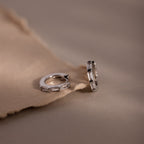 Pair of silver hoop earrings with clear baguette cut gemstones on a soft brown fabric background
