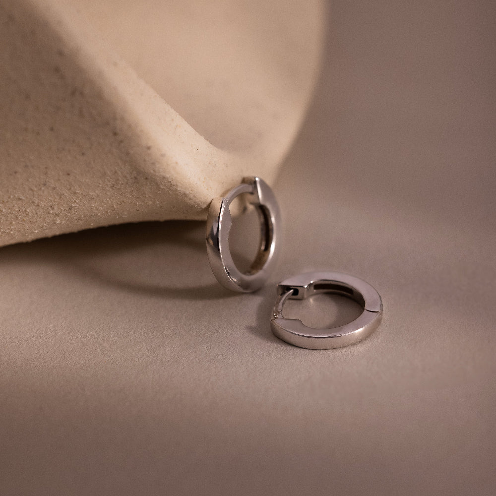 Two small silver hoop earrings on a beige background