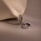 Two small silver hoop earrings on a beige background
